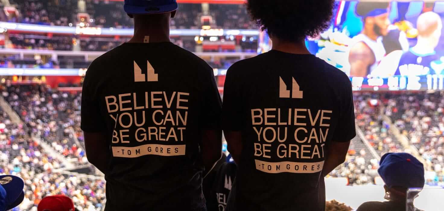Young people watching a basketball game, wearing "Believe you can be great" t-shirts