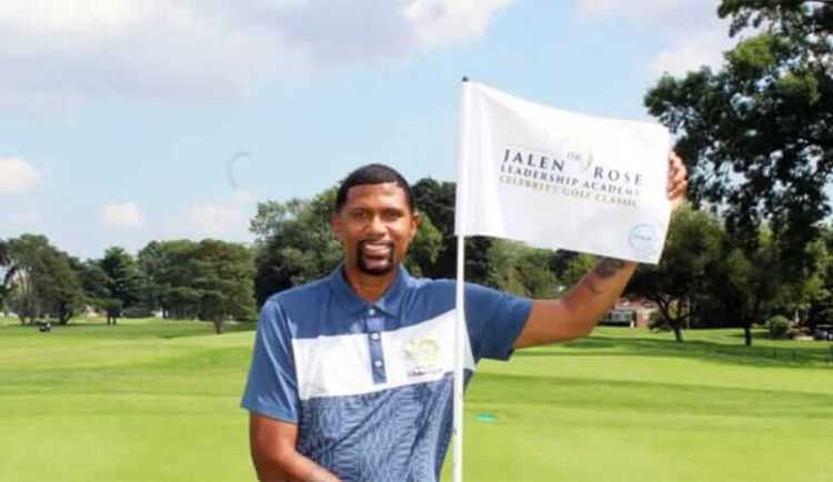 A man standing on a golf course holding a flag for the Jalen Rose Academy
